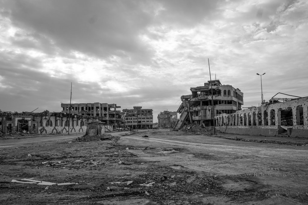 A black and white photo showing the base of the Spring Lady statue surrounded by destroyed buildings in downtown Mosul
