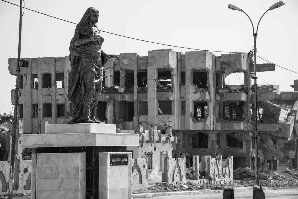 A black and white photo of the newly built Spring Lady statue, with destroyed buildings in the background